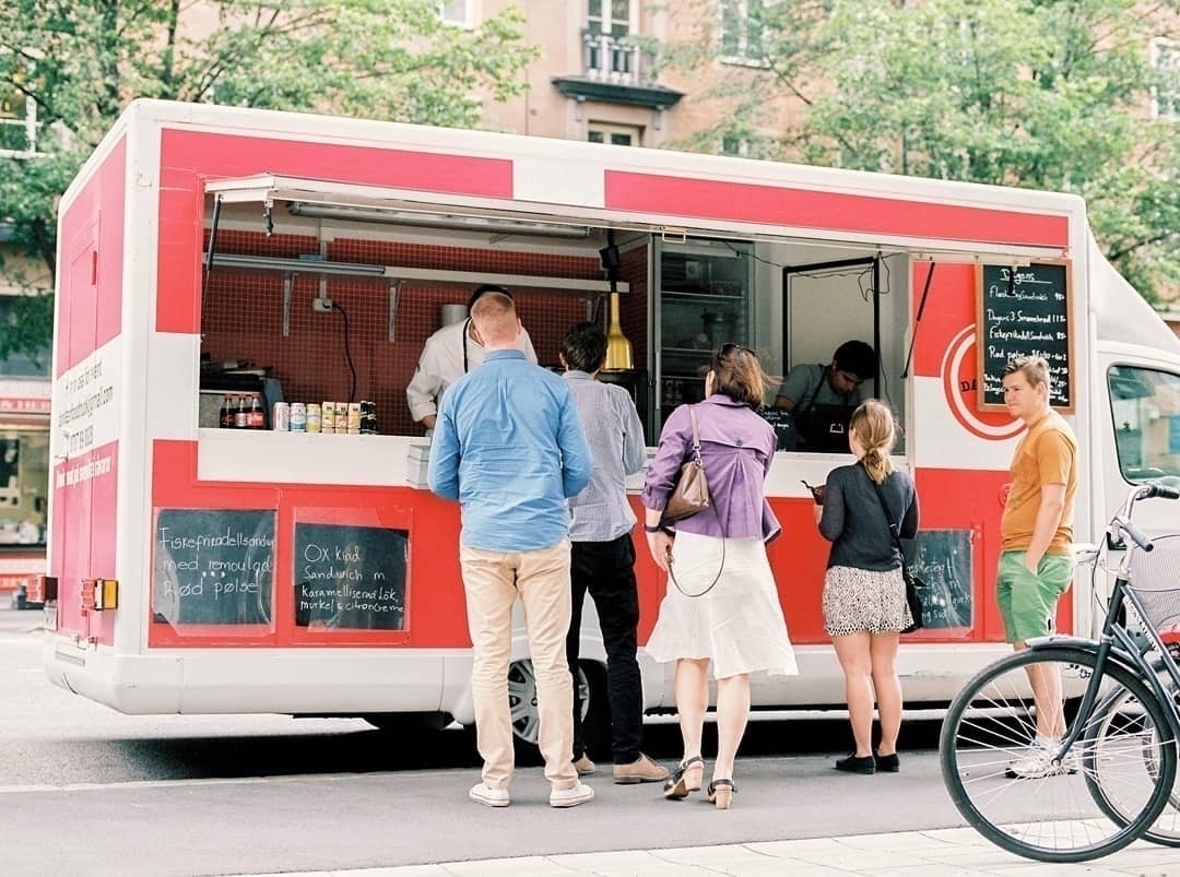 Auto-generated description: A group of people is gathered at a red and white food truck parked on the street, placing orders.