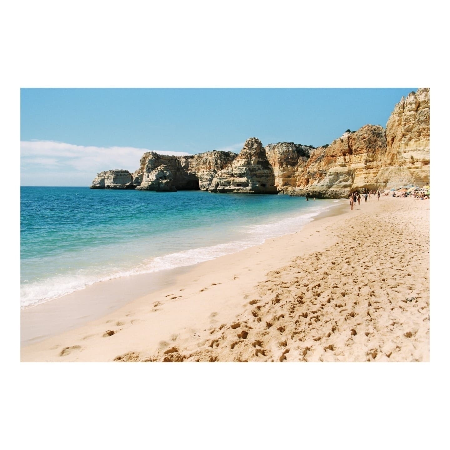 Auto-generated description: A picturesque beach scene features turquoise water, sandy shores, and striking rock formations under a clear blue sky.