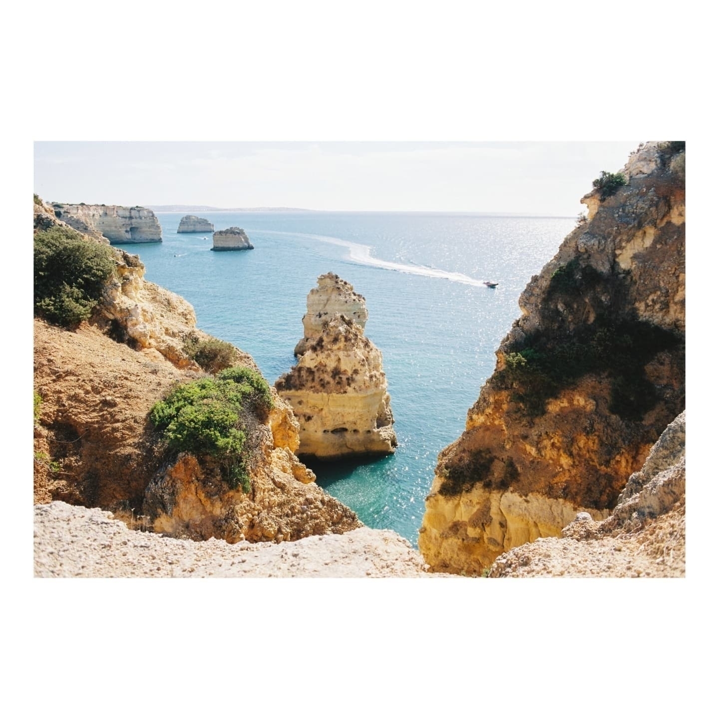 Auto-generated description: A picturesque coastal scene features rugged cliffs, turquoise water, and a distant boat on a sunny day.