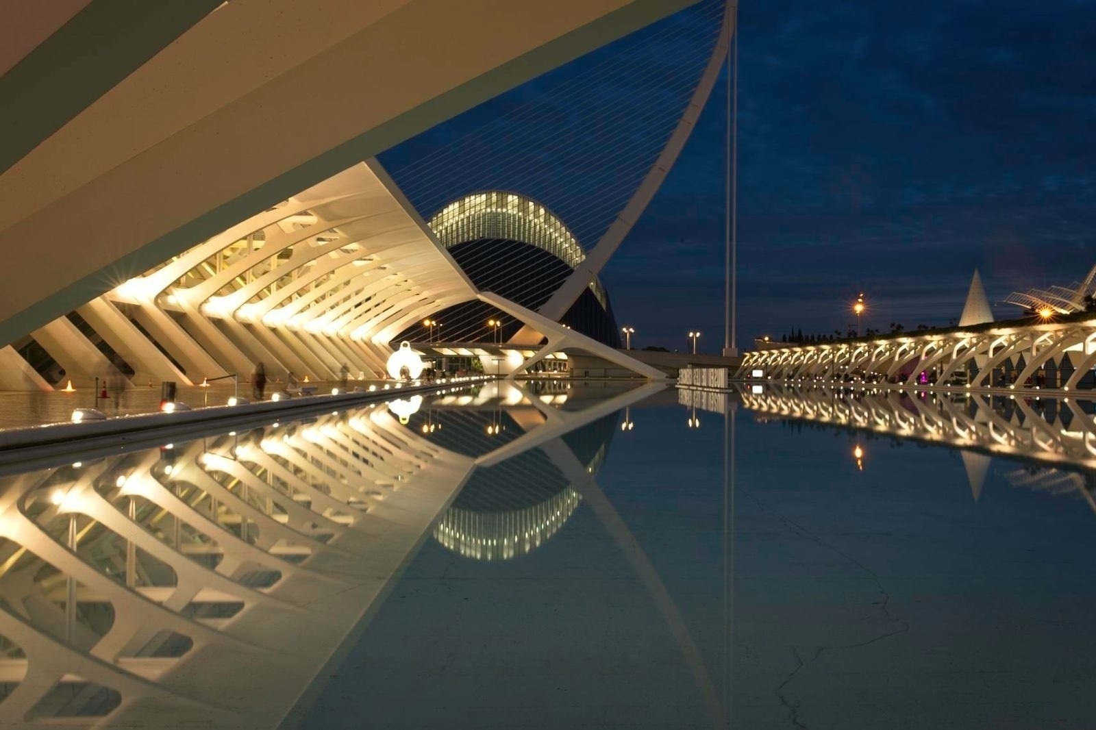 Auto-generated description: Futuristic architectural structures are illuminated at night, reflecting beautifully on a calm body of water.