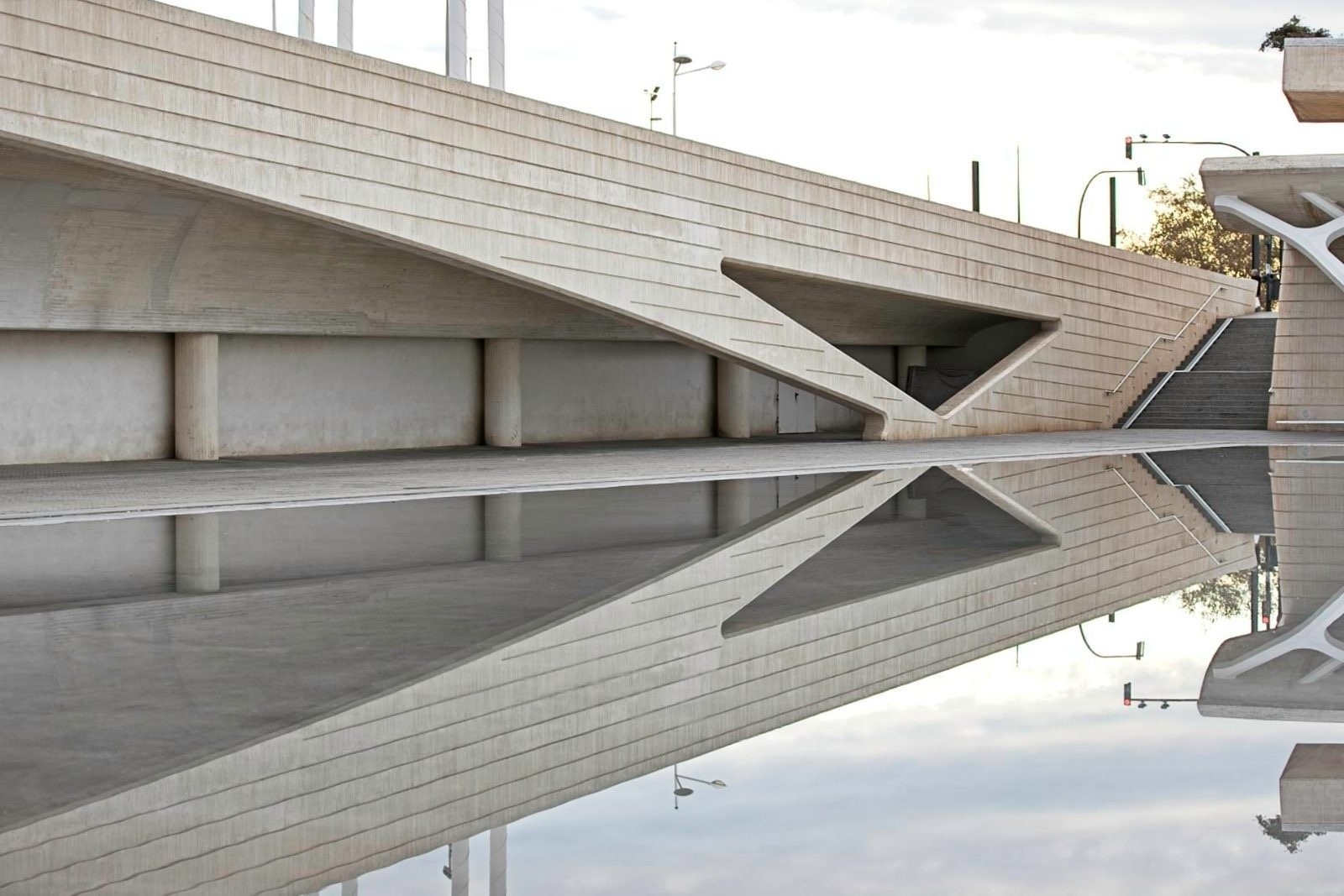 Auto-generated description: A modern architectural structure with clean lines and geometric shapes is reflected in a still body of water.