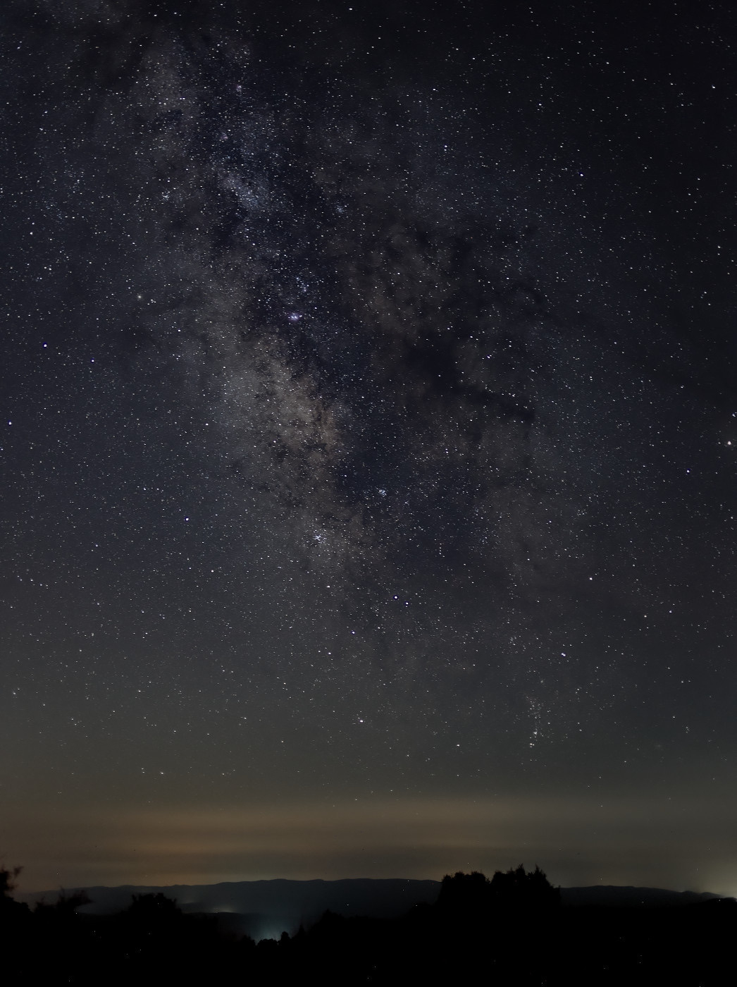 Auto-generated description: A breathtaking view of the Milky Way galaxy is visible above a silhouetted landscape under a clear night sky.
