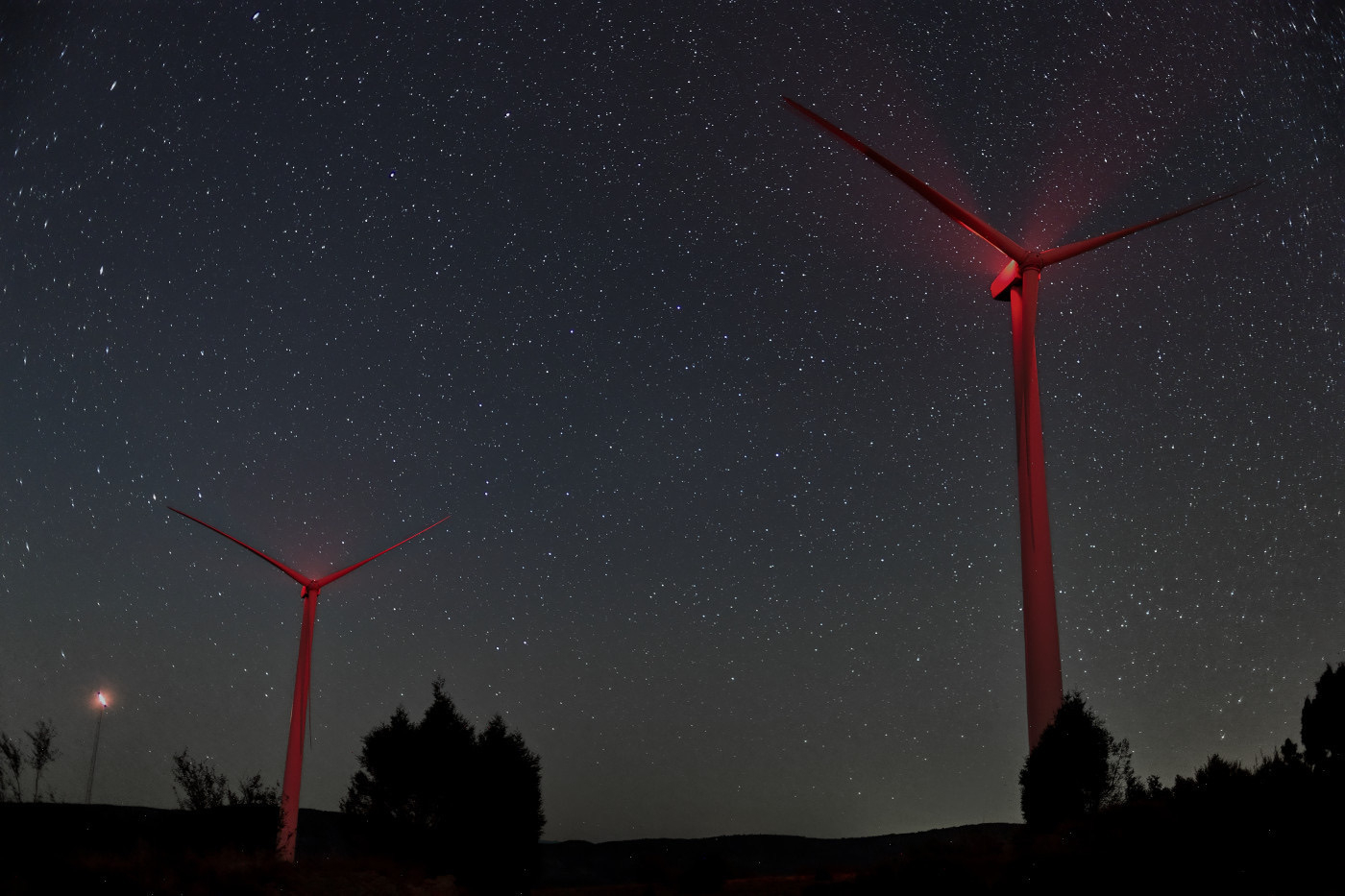 Auto-generated description: Two wind turbines are illuminated under a starry night sky.