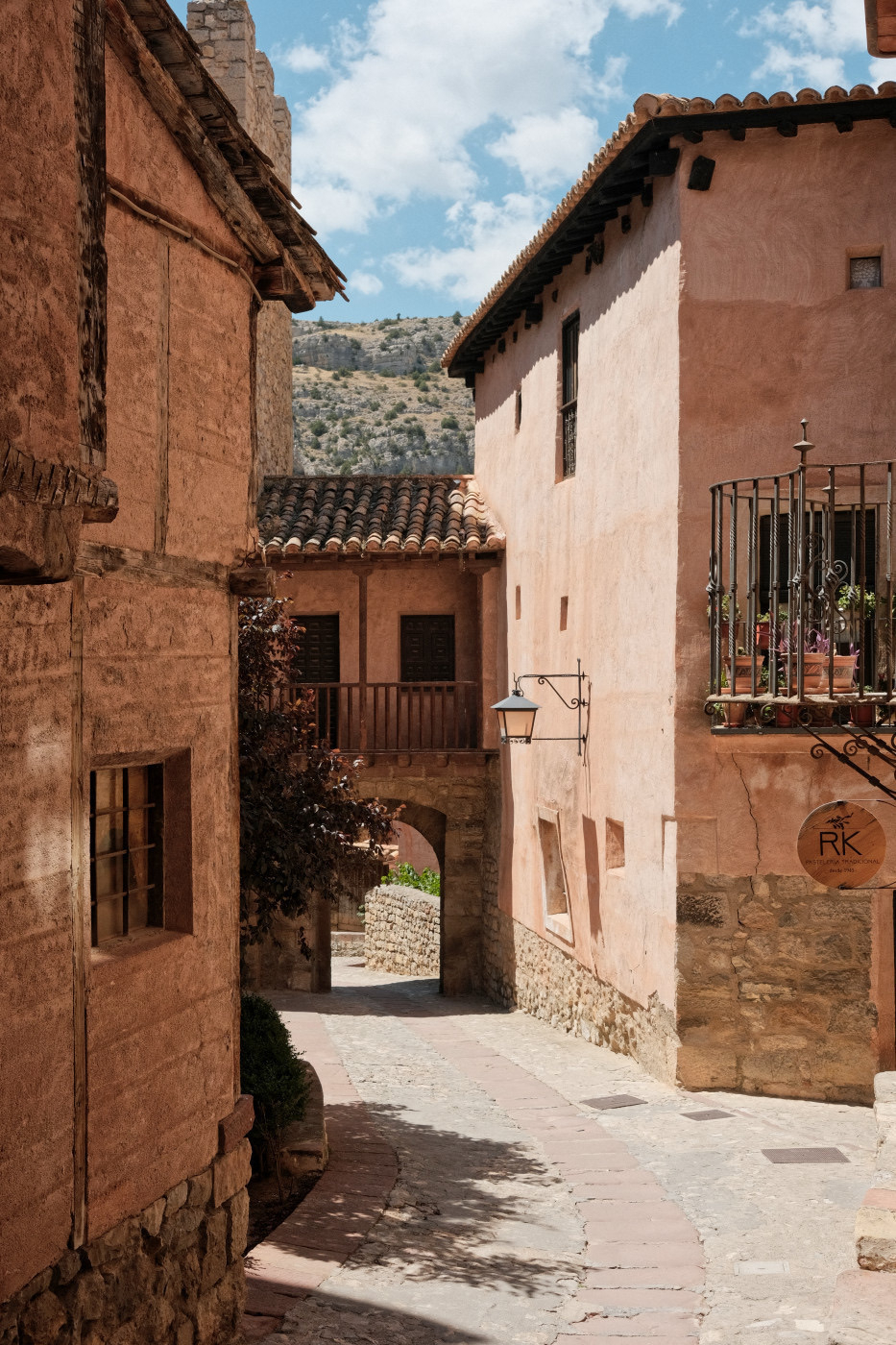 Auto-generated description: A charming narrow street is lined with rustic, pink-hued buildings in a picturesque, old-world setting.