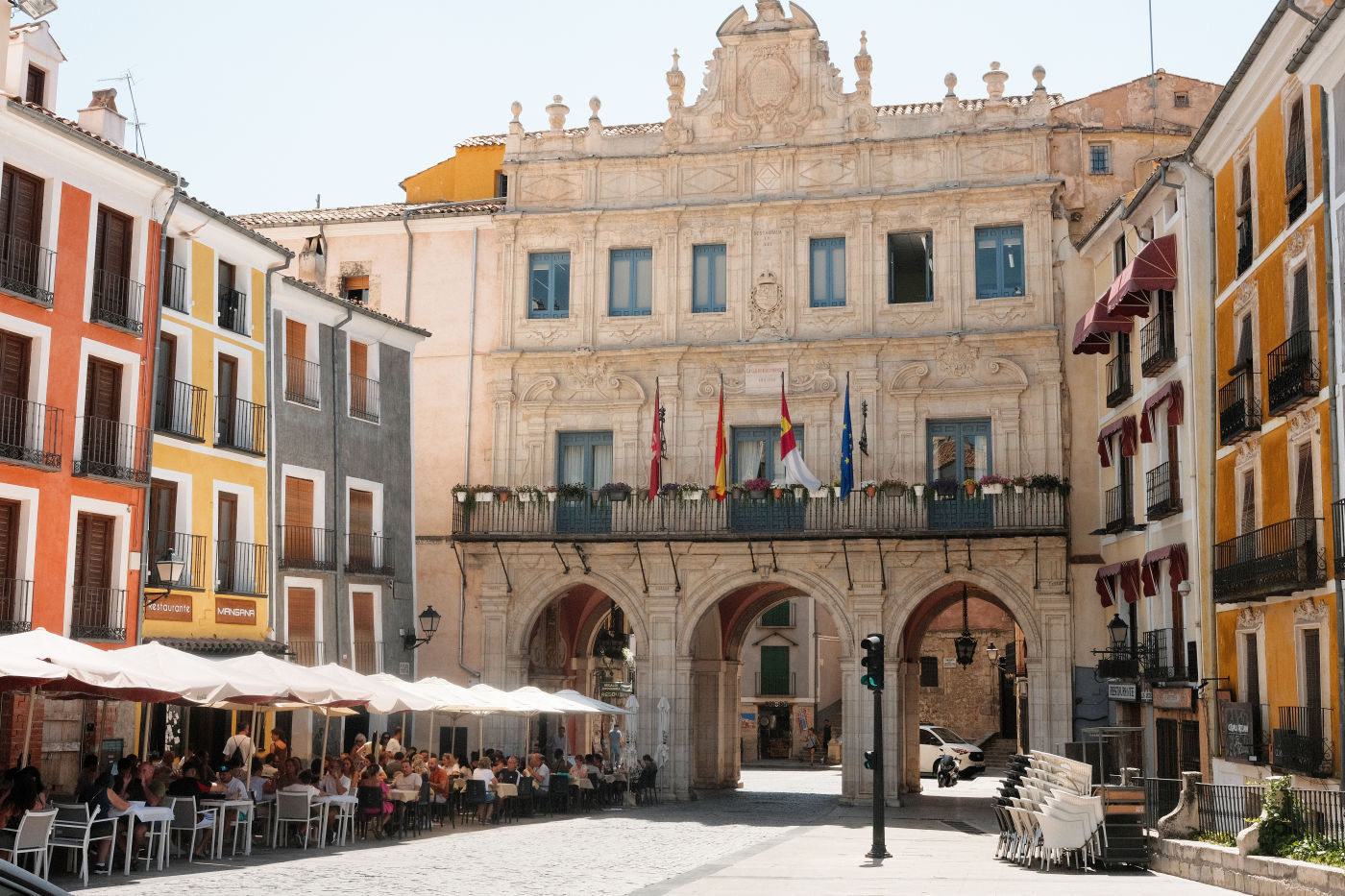 Auto-generated description: A picturesque European plaza features colorful buildings, a historic archway, and outdoor dining with people enjoying a meal.