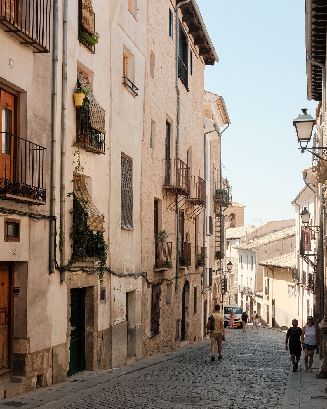 Auto-generated description: A narrow cobblestone street lined with tall, old buildings and a few people walking on a sunny day.