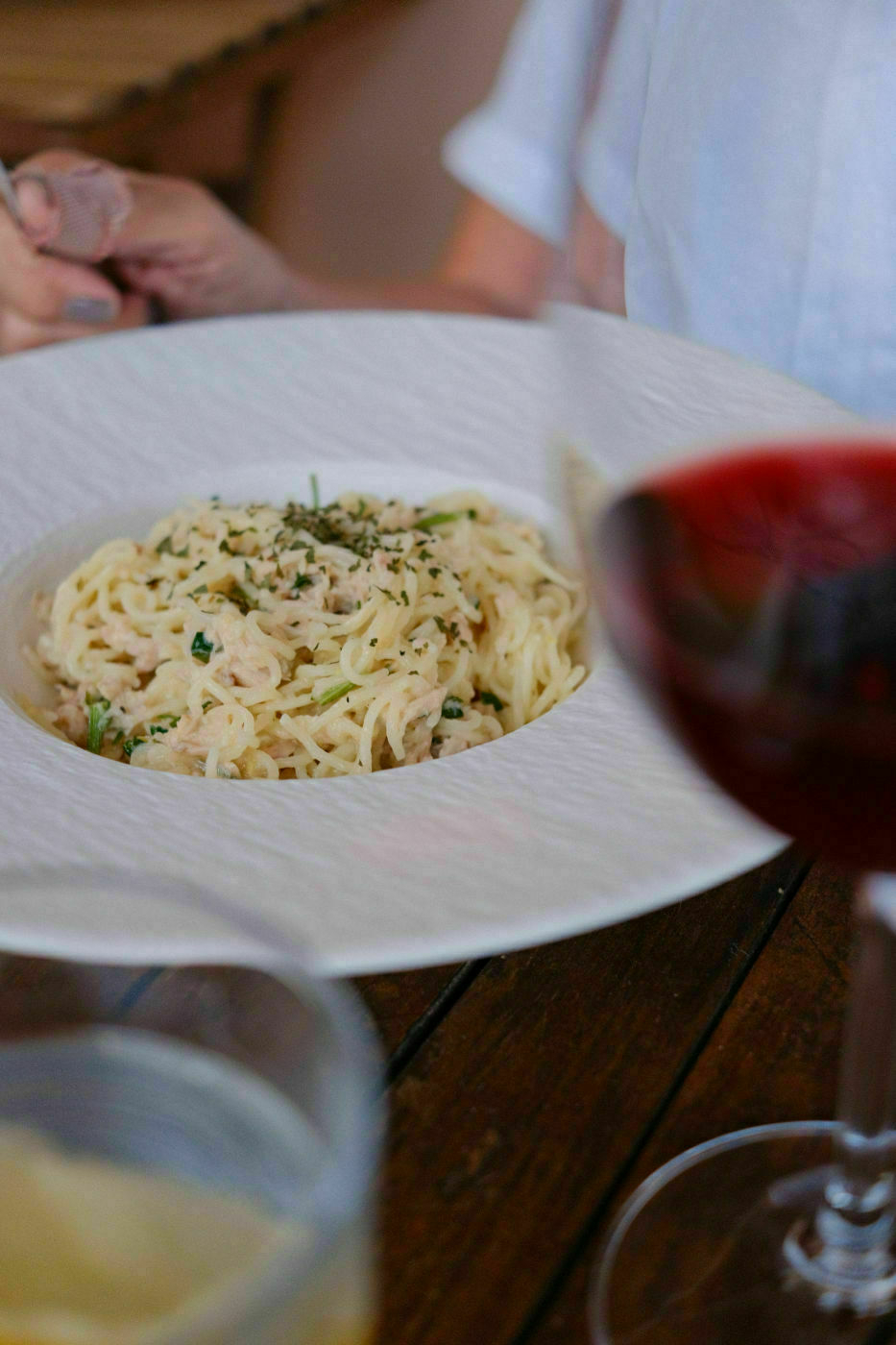 Auto-generated description: A plate of pasta garnished with herbs is served on a table alongside glasses of red wine.